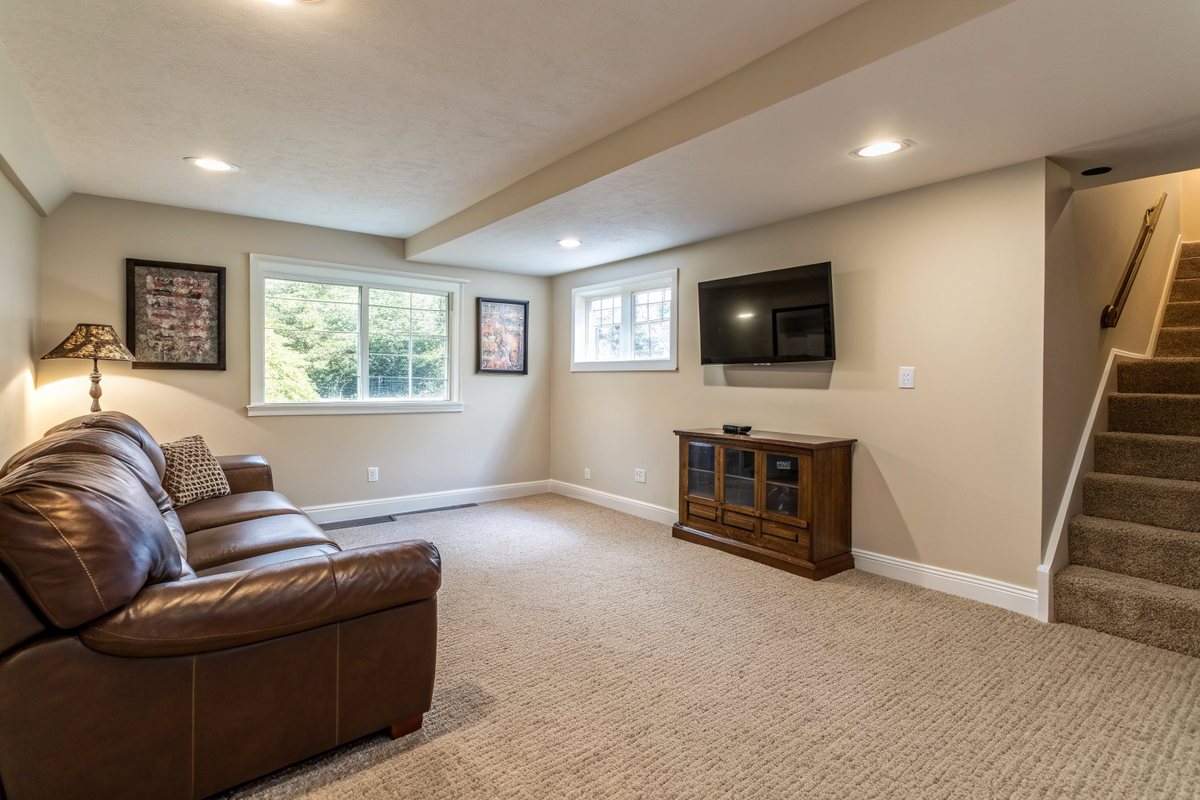 A carpeted finished basement family room with a leather sofa and daylight windows